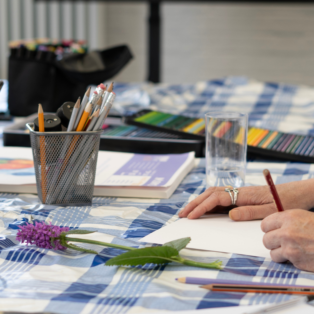 A person's hands drawing a picture with a pencil, and a jar of pencils