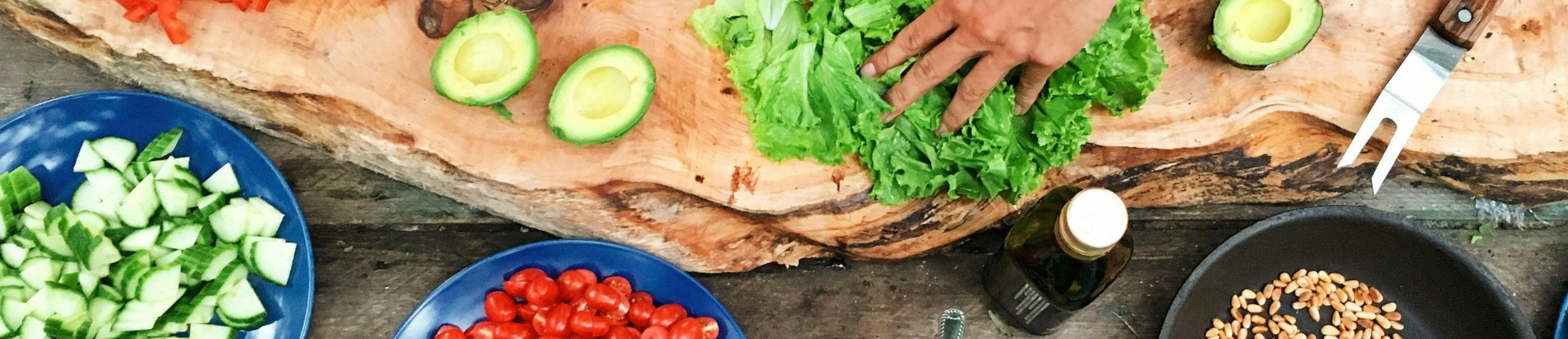 Overhead view of an irregular chopping board and salad ingredients, part of a hand holding lettuce leaves.